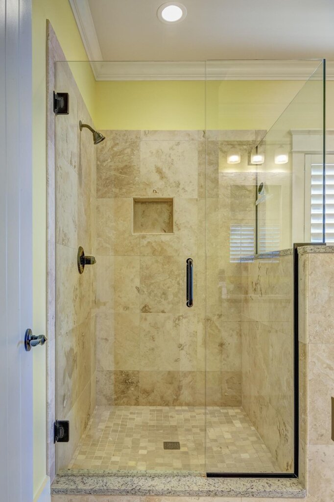 person spraying bathroom cleaner on shower glass door