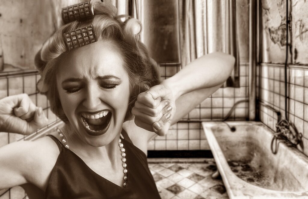 person wearing gloves removing old black silicone caulk with a utility knife in bathroom