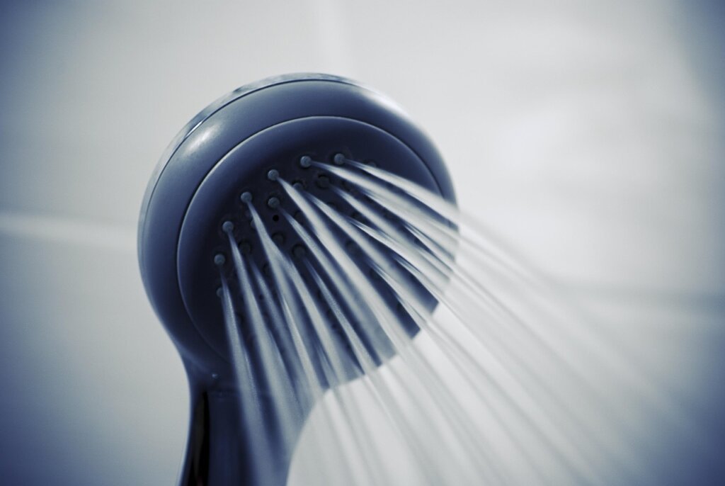 person scrubbing showerhead nozzles with a toothbrush after soaking